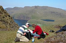 Tourists on a hiking trip south of Fámjin. Kirkjuvatn at right and a part of the village are visible behind them.