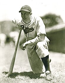 Um jogador de beisebol está ajoelhado com um joelho apoiado em um taco de beisebol.