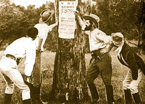 The Kelly gang inspects a reward notice for their capture.