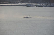 Foto av flyet på elven, midt i bildet, like etter landing, med byen i bakgrunnen.