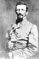 Black and white photo shows a man with moustache and beard. He wears a gray military uniform with two rows of buttons.