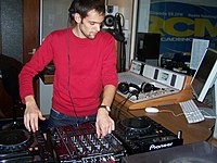 DJ Aron Scott DJing a set for a French radio station. He is using digital CDJ decks instead of phonograph turntables. Aron Rcm.jpg