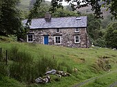 A colour photograph of a stone cottage on a hill.