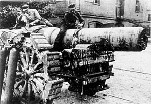 Three men sit on top of a large artillery piece.