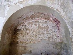 Photographie en couleurs d'une niche dans un mur dont la voûte porte des vestiges de peinture rouge foncé.