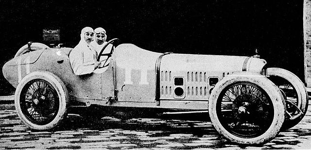 Photo de deux hommes en tenue de pilote prenant la pose dans le cockpit d'une voiture.