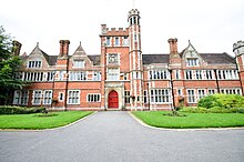 A mock tudor, red brick building with crenellations in white stone and a central tower.