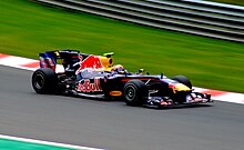A blue and yellow racing car with Red Bull sponsorship being driven on a dry circuit