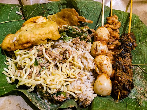 Pecel with fritter, sate puyuh (quail egg satay), sate keong (freshwater snail satay), and sate usus (chicken intestine satay) on a teak leaf in Tuban