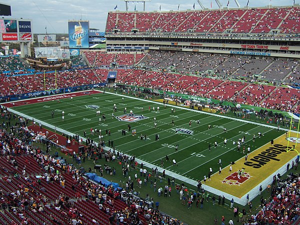 Raymond James Stadium with Super Bowl XLIII decorations and colored lights viewed from nearby parking lot roof.