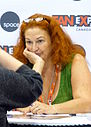 Eine Frau mit roten Haaren, einer Brille auf dem Kopf und einer grünen Scheiße, die mit einer ihrer Hände vor dem Mund sitzt.