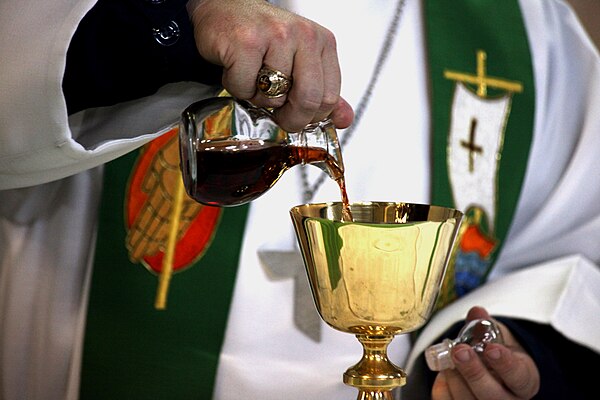 A chaplain pouring sacramental wine from a cruet into a chalice