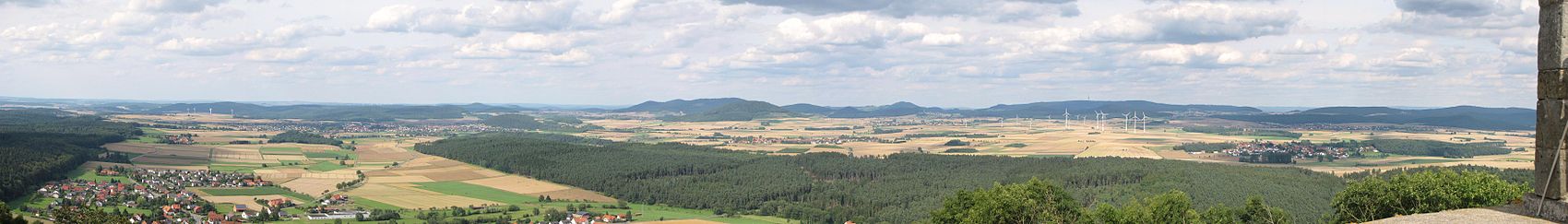 Von der Weidelsburg kann man fast den gesamten Naturpark überblicken. Hier der Nordostblick: Links vorne im Panorama ist Ippinghausen zu erkennen. Schräg rechts darüber sieht man Wolfhagen. Am Horizont in der Bildmitte ist der Große Bärenberg mit Funk- und Aussichtsturm zu erkennen. Weiter rechts oberhalb der Windkraftanlagen liegt der Habichtswald