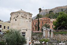 View in 2021. The acropolis rises behind. The fragments of a porch are set up to the right, between the visitors, and the remains of the Roman aqueduct are at far right 20211102 224 athenes.jpg