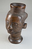 Head goblet (Mbwoongntey); 19th century; wood; Brooklyn Museum. It has one-inch cylindrical lip with linear decoration. The hair is made up of crosshatched lines with a raised diamond-shaped segment on the back of the head. Its cheeks have curved multilinear scarification