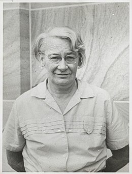 Dorothy Hill, later in life, standing before a sandstone wall.jpg