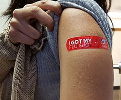 ドラッグストアにおいてワクチン接種を受けた後、接種位置を見せるアメリカ人女性