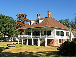 A two story house with a large porch upstairs, two chimneys, and a lot of trees behind it.