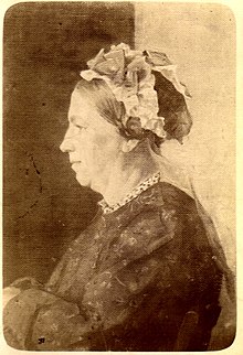 Photograph of Louise Milliet, from the side. She is seated, wearing a dress, with flowers in her hair.