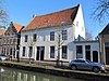 Groot dwarshuis met zadeldak en gepleisterde lijstgevel. Het achterhuis staat haaks op het voorhuis en heeft een gepleisterde puntgevel. Vormt een geheel met het buurnummer 19