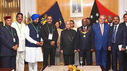 The governor-general of Papua New Guinea with the president of India, and other diplomats, standing under a portrait of the Queen at Government House, Port Moresby[20]
