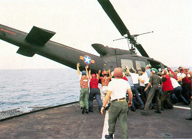 An empty Huey helicopter is jettisoned over the side of a carrier to provide room on the ship's deck for more evacuees to land.