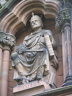 Sittende steinstatue av en mann med krone i kappe og med et sverd i den ene hånden og en bok i den andre.