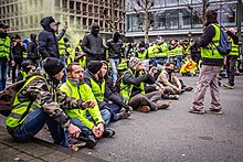 Encuentro de chalecos amarillos en Bruselas, principalmente hombres.  Algunos están sentados en primer plano.