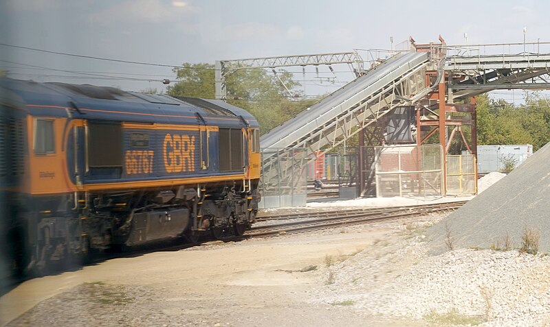 File:66767 moves slowly under the Ely Papworth aggregates loader.jpg