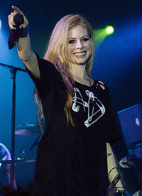 A blode woman in a black t-shirt smiling while holding her microphone towards the crowd