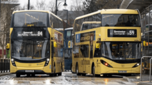 Two yellow double-decker buses with Bee Network logos in a rainy bus station