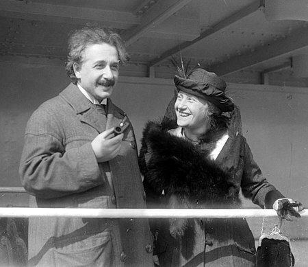 Einstein, looking relaxed and holding a pipe, stands next to a smiling, well-dressed Elsa .