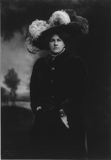 Opera singer Emmy Destinn wearing a plume-covered hat, around 1909. Emmy Destinn, 1878-1930, three-quarters length portrait, standing, facing left, wearing fur hat.jpg
