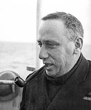 Informal head-and-shoulders portrait of man in dark coat and sweater, smoking a pipe
