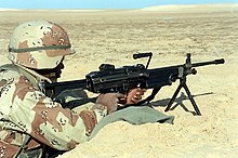 A U.S. Marine with an M249 SAW on its bipod manning a foxhole during the Persian Gulf War