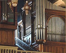 The metal pipes of two organs are in wooden cases of different dates and styles in the organ loft. To the side of the organ is a mosaic showing God as creator.