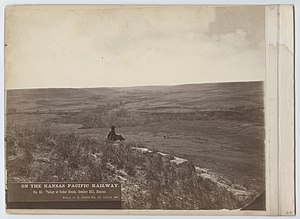 Photographer Robert Benecke seated upon an outcrop of the Fencepost limestone. (1873) No. 40. Valley of Cedar Creek, Bunker Hill, Kansas. (6860558710).jpg