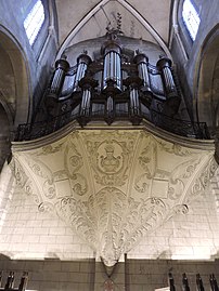 Photo d'un orgue en position haute, sous la voute d'une église. Il est supporté par un piédestal ouvragé.