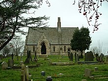 Eine kleine Steinkirche von Süden gesehen mit einem weitläufigen Dach, kleinen Lanzettenfenstern, einer markanten Giebelveranda und einer zentralen Glocke