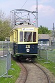 Foto a colori di un tram elettrico montato anteriormente su rotaie, il tetto è grigio, l'auto è beige in alto e blu in basso.