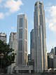 Ground-level view of several skyscrapers; the building on the right is the tallest and has a square cross section with several diagonal protrusions. A shorter building on the left resembles it closely.