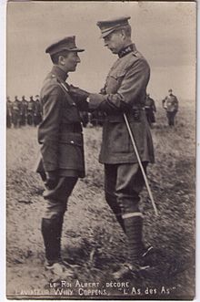 Photographie noir et blanc de deux hommes en uniforme, le premier décorant le second. En arrière plan, des hommes en uniforme observent la scène.
