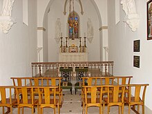 Wewnątrz kaplicy ławki kościelne, knajpa, ołtarz witrażowy i świeczniki liturgiczne.
