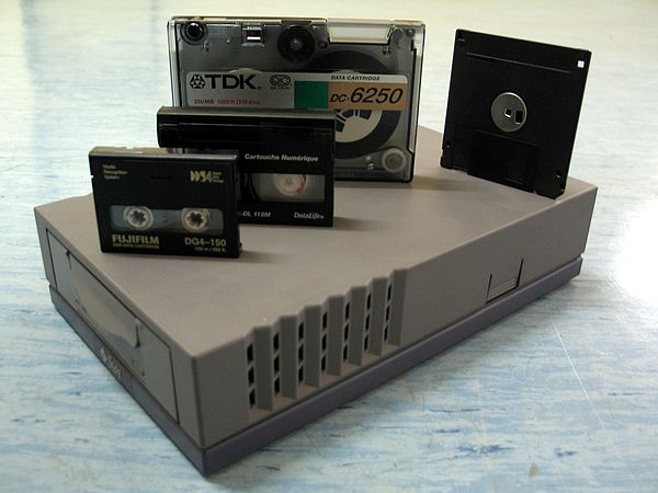 DDS tape drive. Above, from left to right: DDS-4 tape (20 GB), 112m Data8 tape (2.5 GB), QIC DC-6250 tape (250 MB), and a 3.5" floppy disk (1.44 MB)