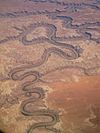 View from an airplane: A river meanders this way and that through a reddish-brown landscape.