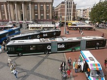 Biarticulated low-floor bus with text written in Dutch on, along with other articulated bus.