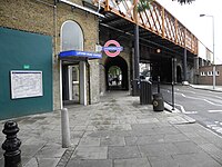 A railway on a brick viaduct crosses a road, an entrance in the brickwork below a sign reading "LATIMER ROAD STATION"