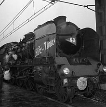 Photographie en noir et blanc d'une locomotive à l'arrêt avec des inscriptions blanches à l'avant.