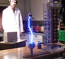 A small demonstration Marx generator (tower on the right). It is a ten stage generator. The main discharge is on the left. The nine smaller sparks that can be seen in the image are the spark gaps that connect the charged capacitors in series. Marxgeneratorfz.JPG