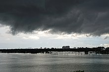 Dark storm clouds over a waterbody with buildings in the far background